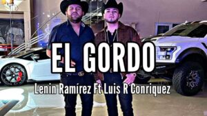 Fotografía promocional de dos hombres con sombreros vaqueros y ropa oscura posando entre un coche deportivo blanco y una camioneta todoterreno en un garaje de lujo con el título EL GORDO en letras grandes y texto de crédito de artistas, ¿Quién ganó al elegir entre Bonoloto y El Gordo de la Primitiva?